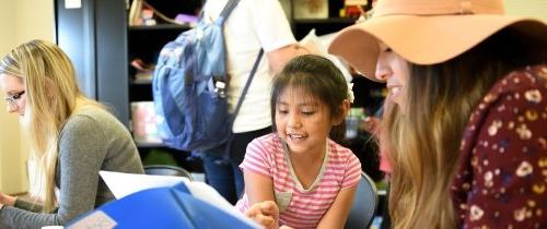 Student teaching a young girl in an after school program